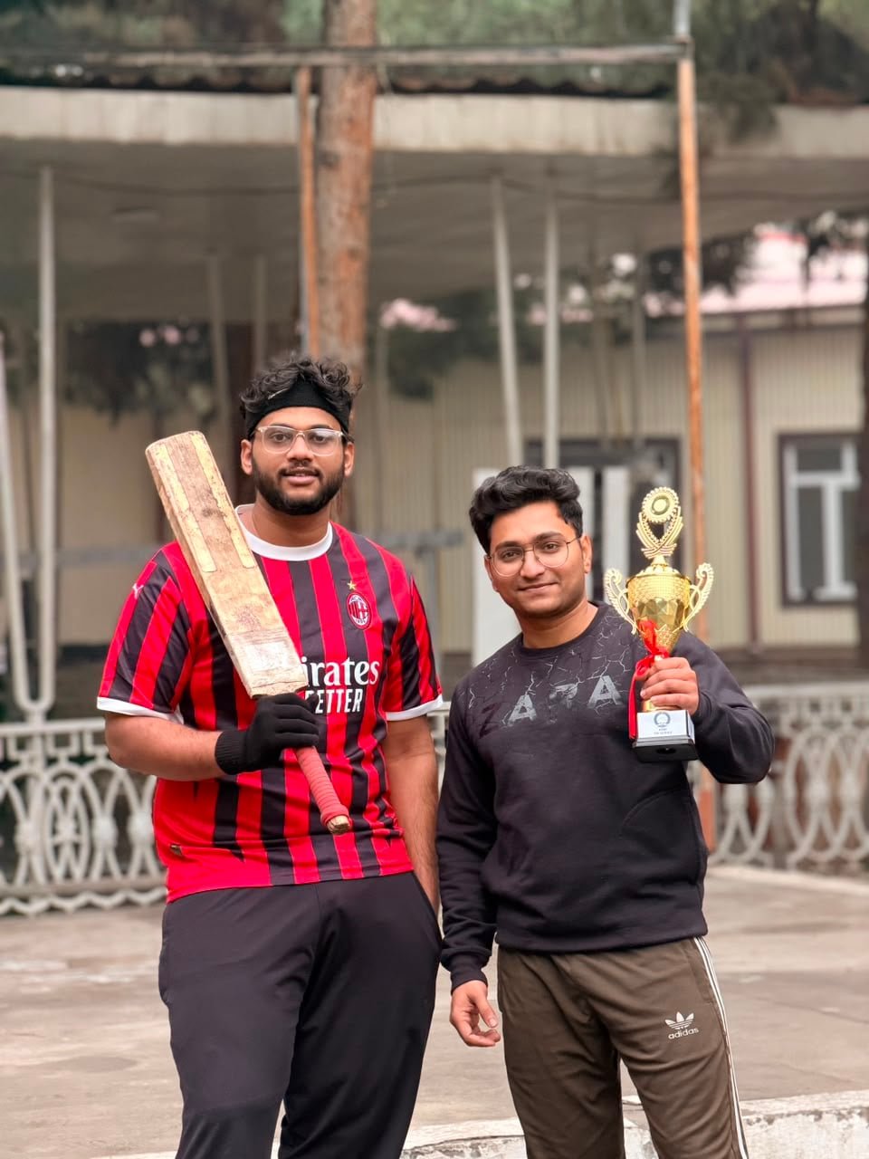 Students with a cricket bat and winners' trophy on campus